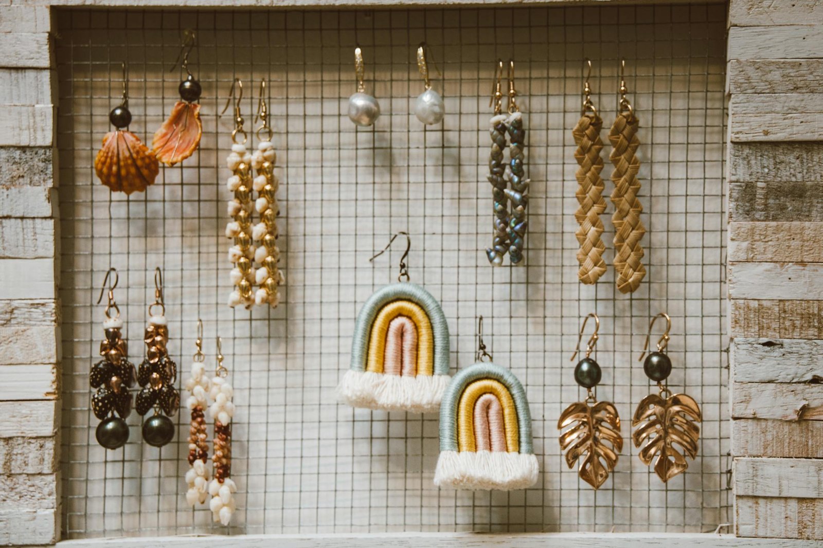 A stylish collection of handmade earrings displayed in a rustic wooden frame with a grid backdrop.