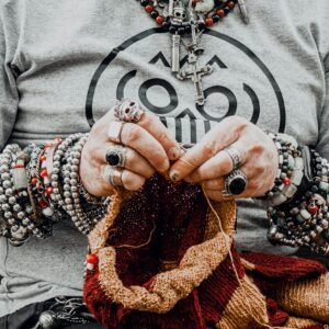 Close-up of a person knitting with hands adorned with rings and bracelets, showcasing elaborate jewelry designs.