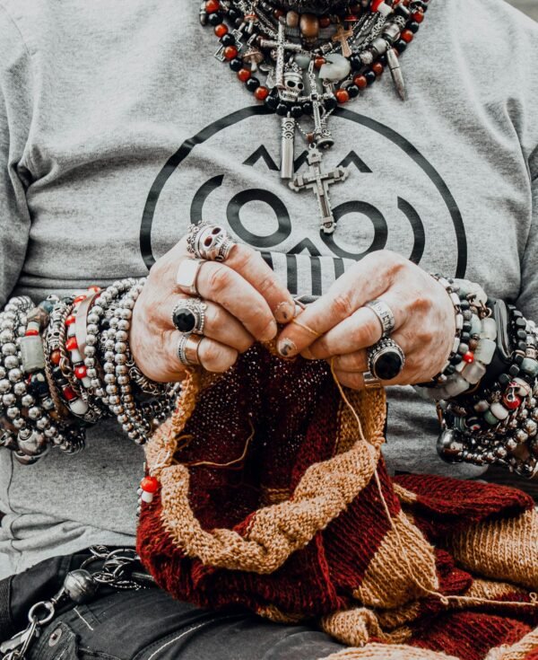 Close-up of a person knitting with hands adorned with rings and bracelets, showcasing elaborate jewelry designs.