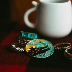 Close-up of artistic jewelry and a white mug on a checkered surface in warm light.