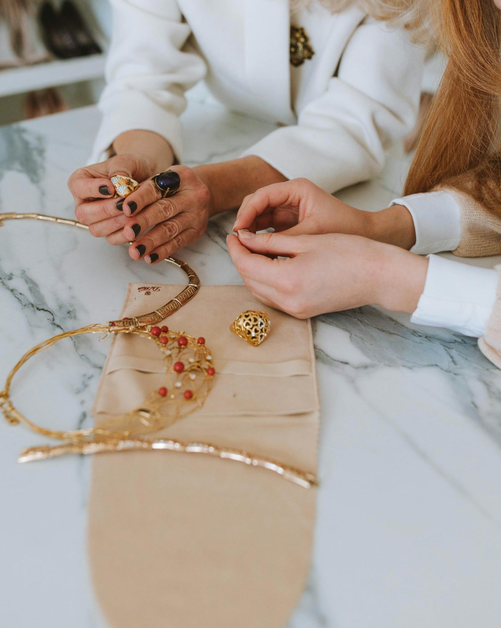 Close-up of hands examining elegant jewelry on a marble table, showcasing craft and detail.