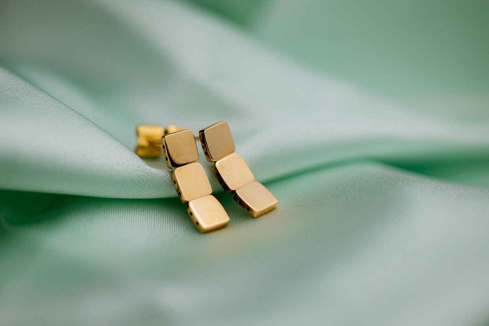 Handcrafted gold earrings resting on a soft green fabric background. Perfect for fashion and style concepts.